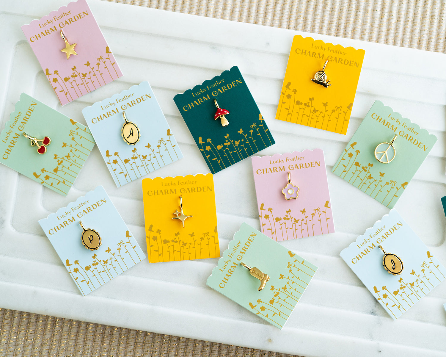 An assortment of Lucky Feather Charm Garden charms are displayed on their colorful backing cards within a white tray.