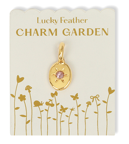 A gold charm with a pink gem on a card labeled 'Lucky Feather CHARM GARDEN.'