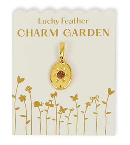 A gold charm with an orange stone on a 'Lucky Feather Charm Garden' card.