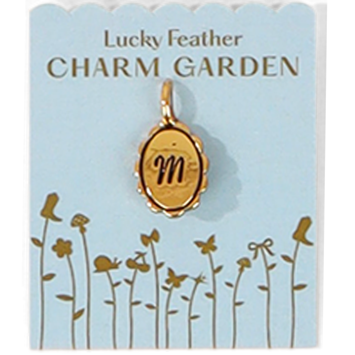 A gold charm pendant with the letter 'm' on a blue card with a garden illustration and the words 'Lucky Feather CHARM GARDEN'.