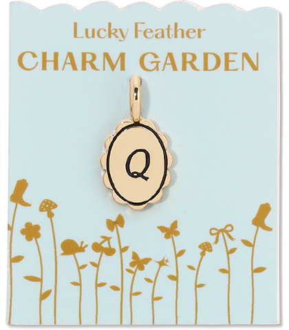 A gold-colored charm with the letter "Q" hangs from a blue card that reads "Lucky Feather CHARM GARDEN" and features illustrations of flora and fauna.