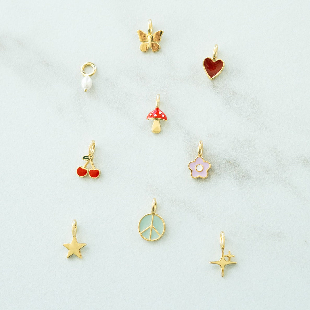 Nine gold jewelry charms with various designs are arranged on a light-colored surface.