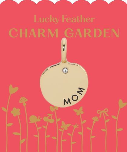 A gold "mom" charm with a gemstone on a pink card featuring flowers.