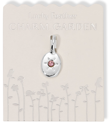 A silver "Lucky Feather Charm Garden" pendant with a pink stone on a white card with an embossed floral design.