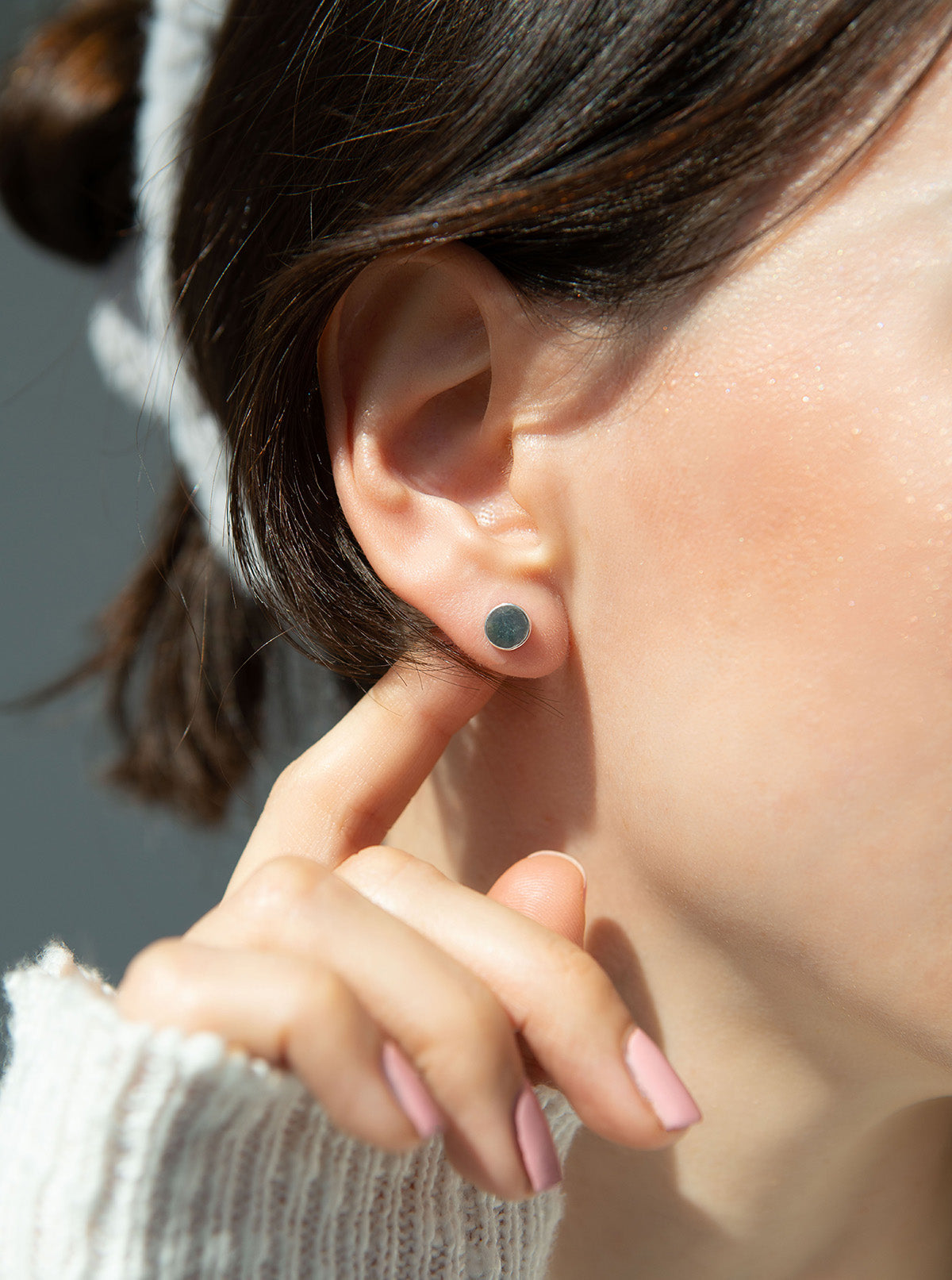 A person touches their ear with a small, round stud earring.