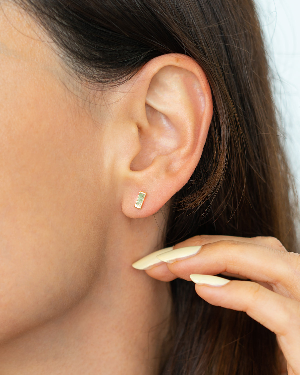 Close-up of a woman's ear with a rectangular gold stud earring.