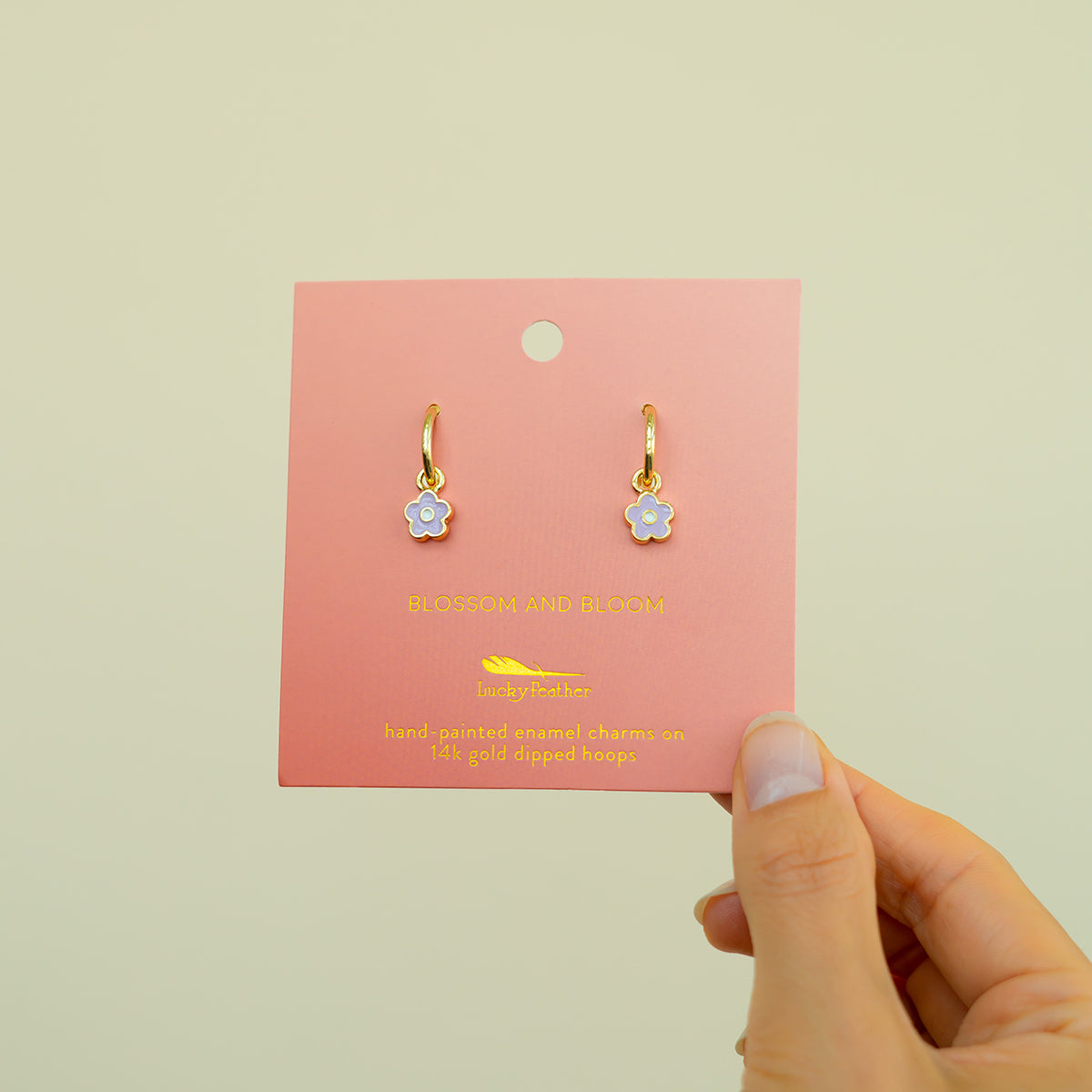 A hand holds earrings displayed on a pink card.