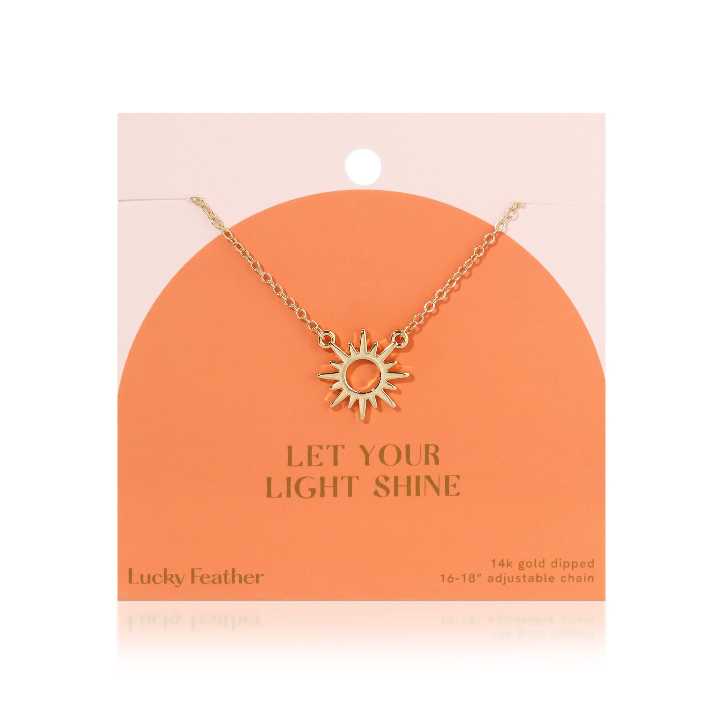 A gold-colored sun pendant hangs on a chain from a peach-colored display card that reads "Let Your Light Shine".