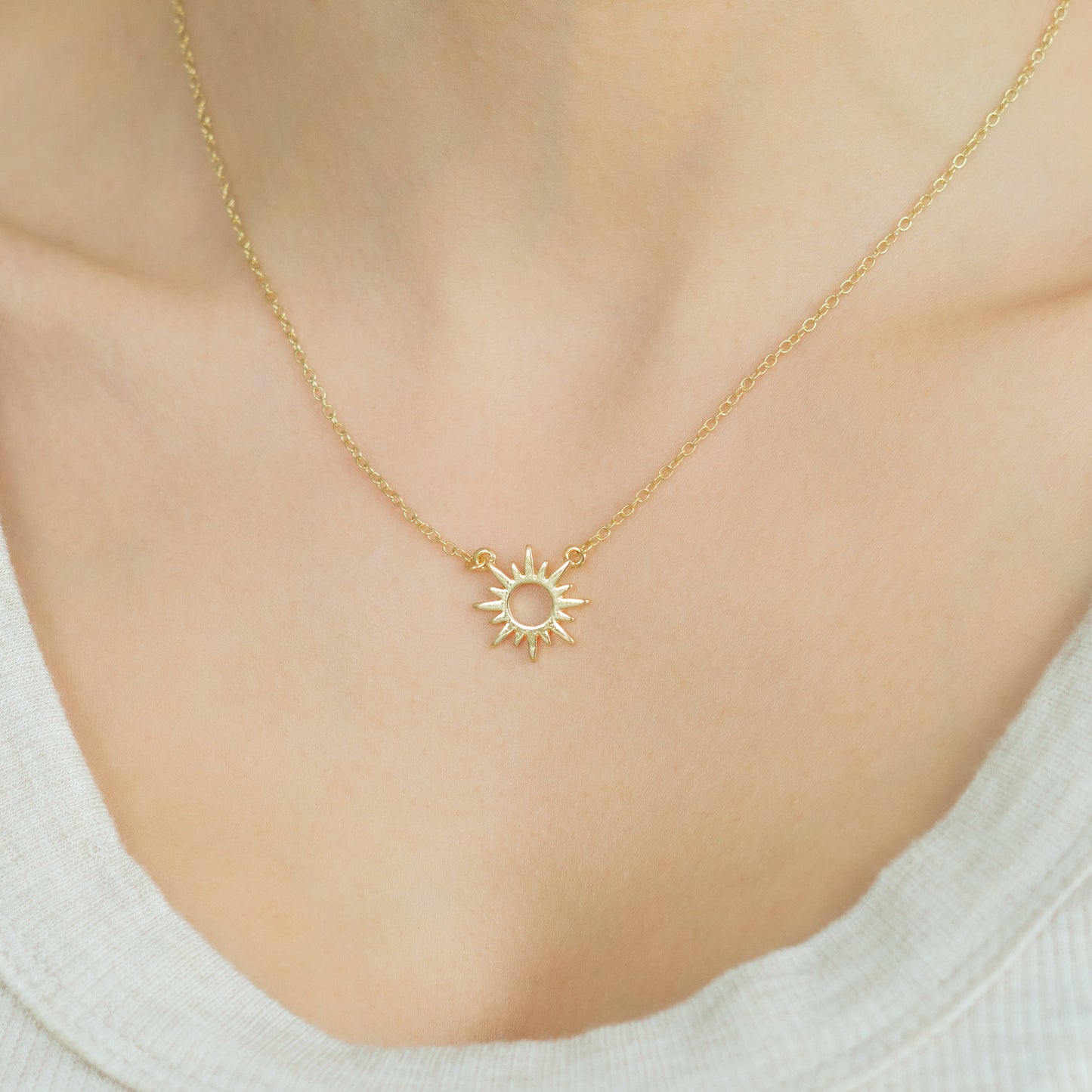 A person wears a gold sun pendant necklace.