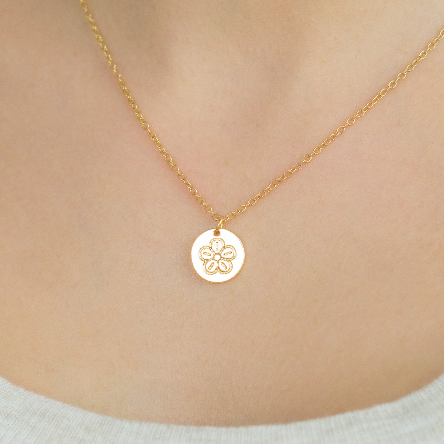 Close-up of a person wearing a gold necklace with a circular flower pendant.