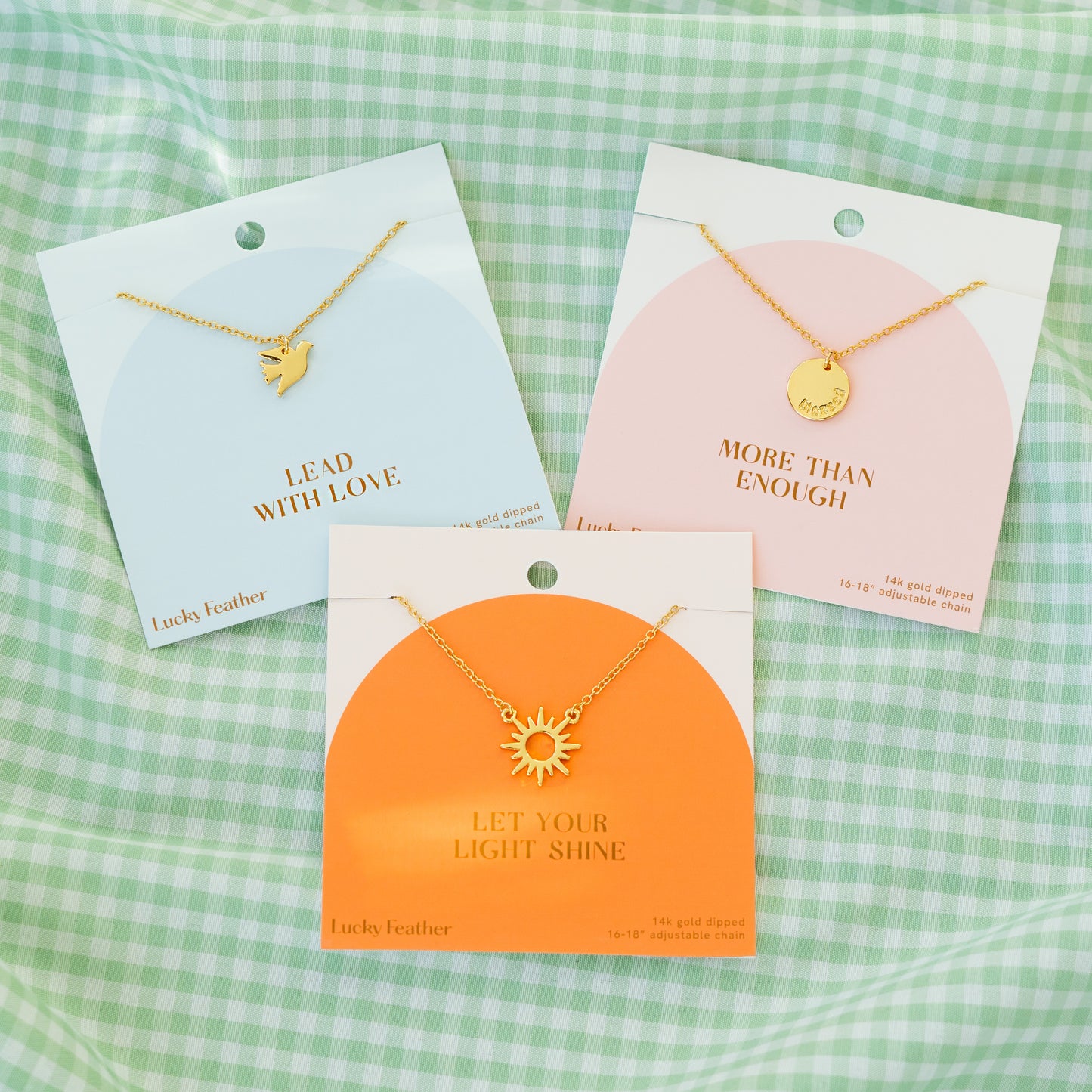 Three necklaces with different pendants are displayed on cards against a green and white checkered background.