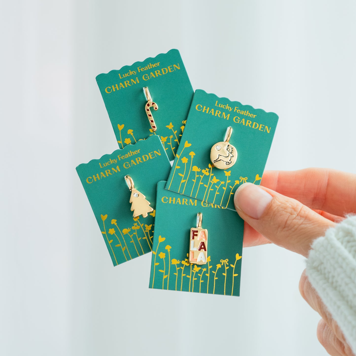 Hand holding four "Lucky Feather Charm Garden" jewelry charms with Christmas themes.