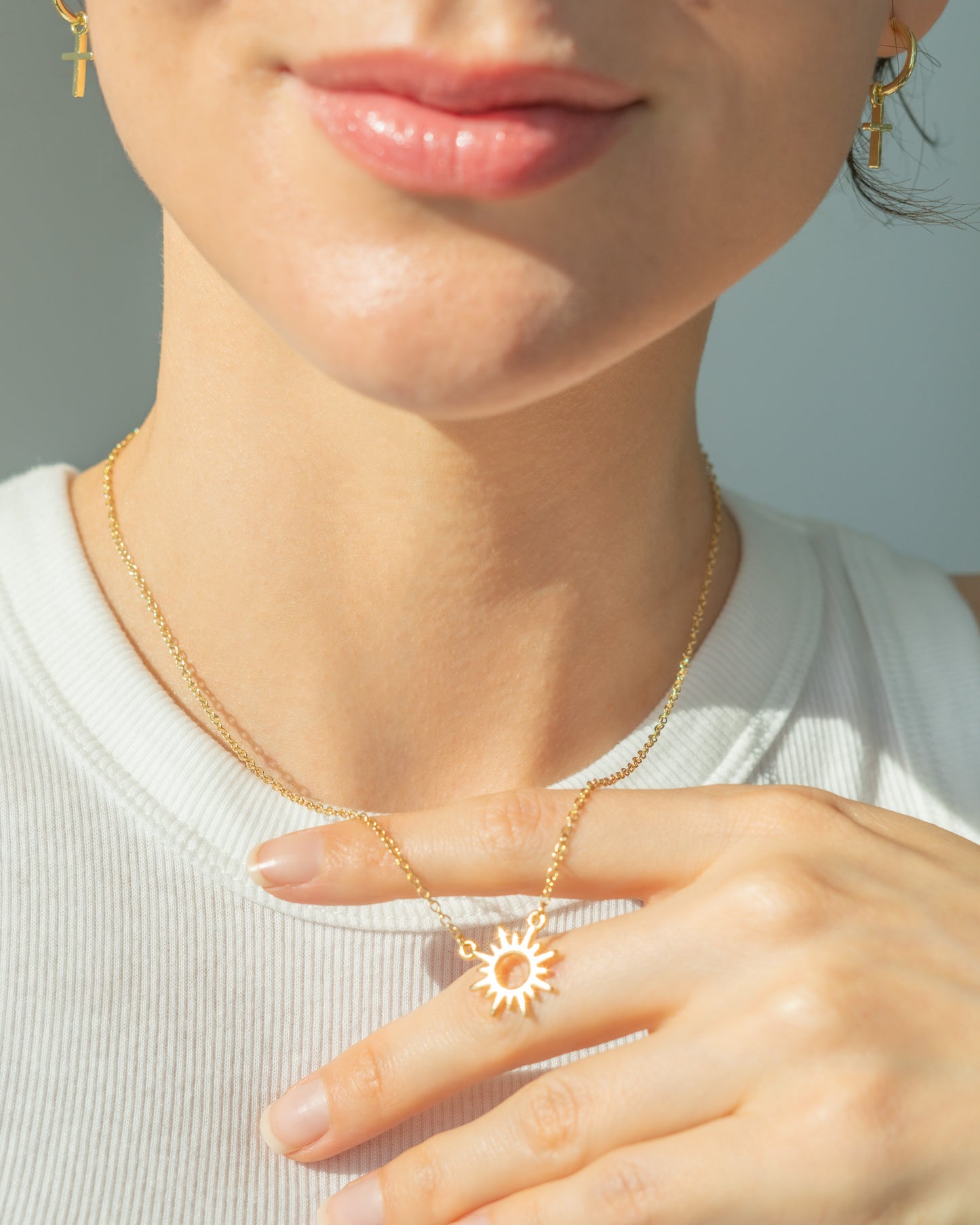 Close-up of a woman wearing a gold sun pendant necklace and cross earrings.