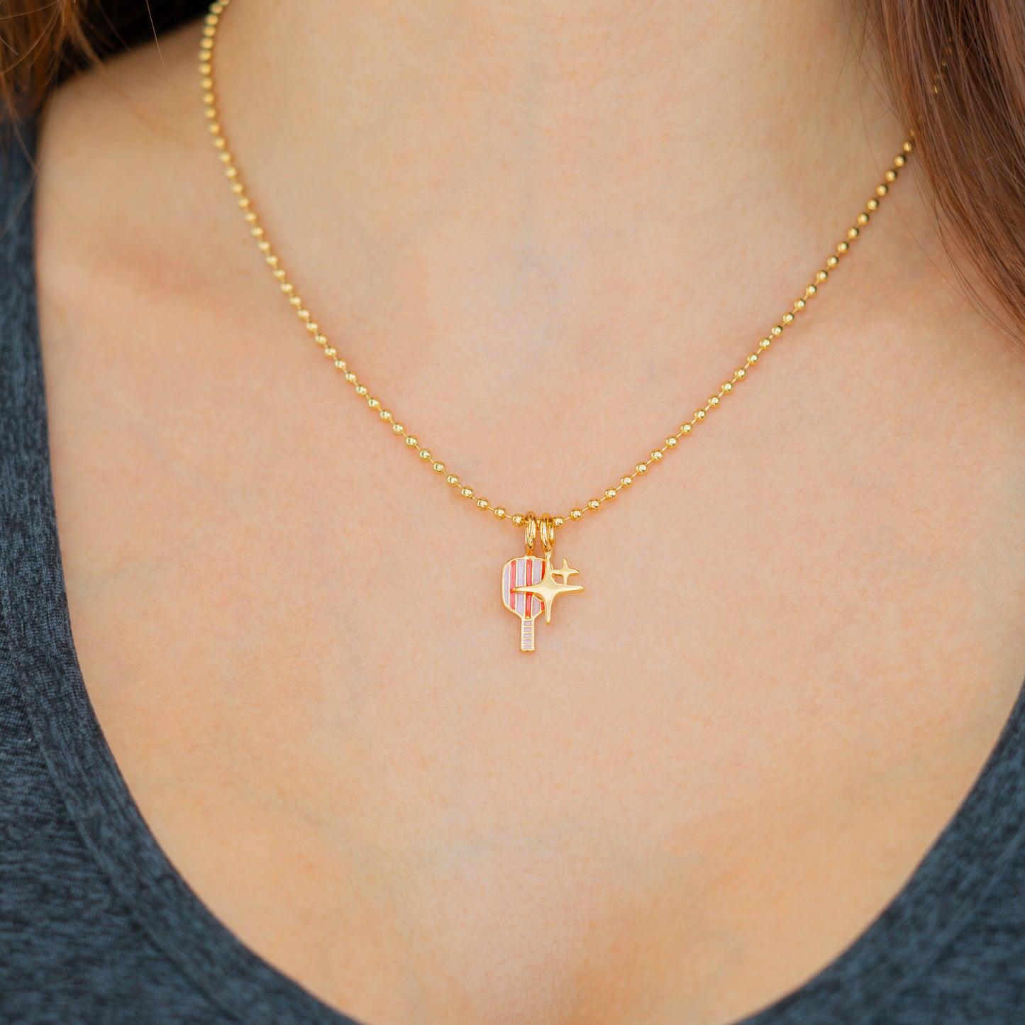 A woman wears a gold bead necklace with a paddle and star charm.