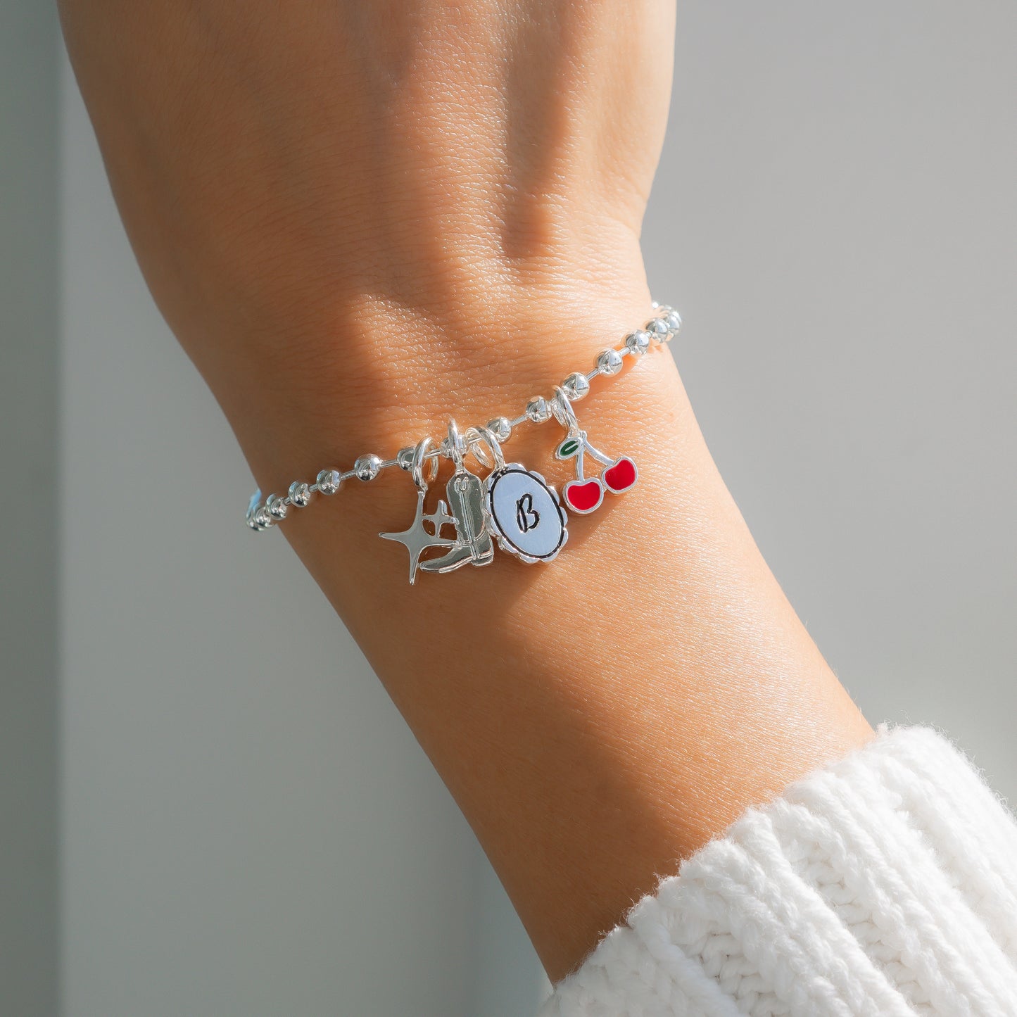 Close up of a wrist wearing a silver charm bracelet with star, boot, initial and cherry charms.