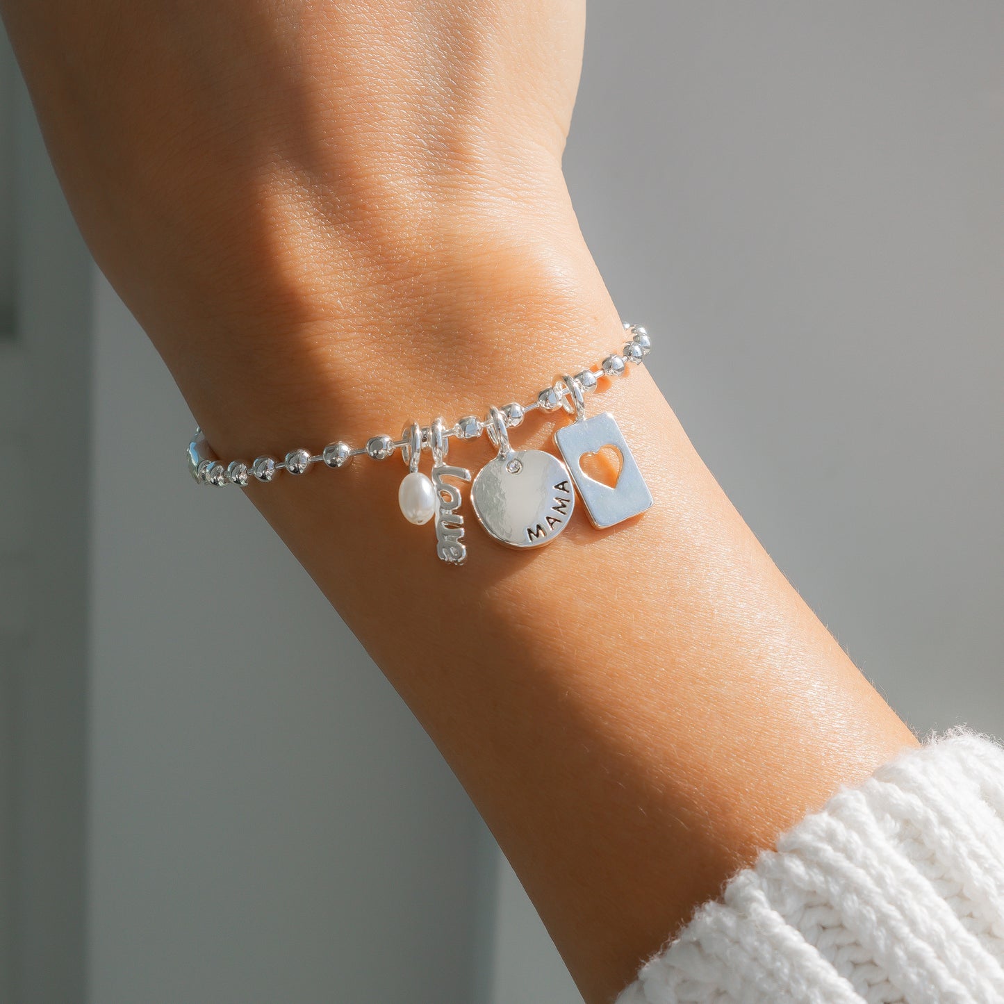 A silver charm bracelet is displayed on a person's wrist.