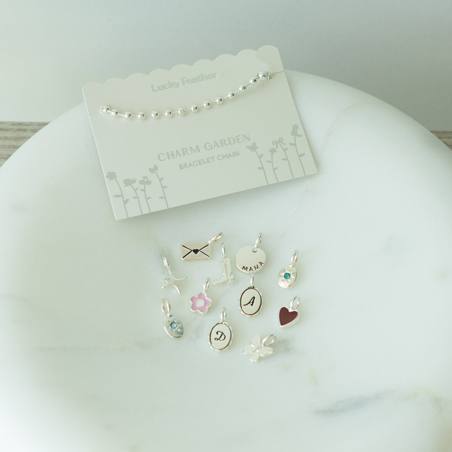 A "Lucky Feather" bracelet chain and various charms arranged on a marble surface.