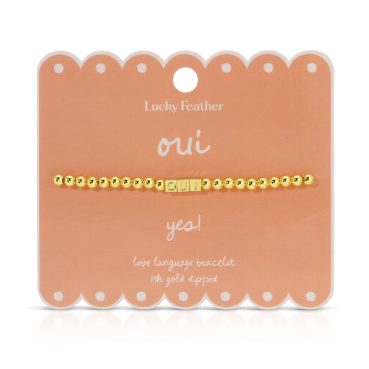The image shows a gold-colored beaded bracelet with the word 'OUI' spelled out in letter beads, displayed on a peach-colored product card.