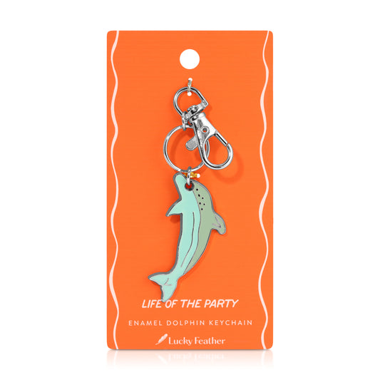 A light blue enamel dolphin keychain hangs on an orange card.