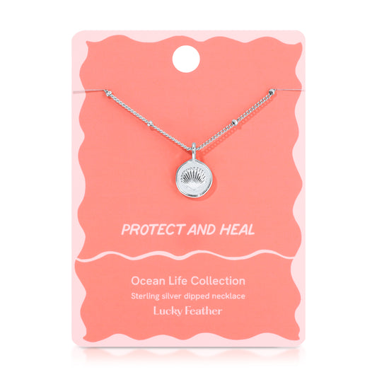 A silver necklace with a round seashell pendant displayed on a pink and white card.
