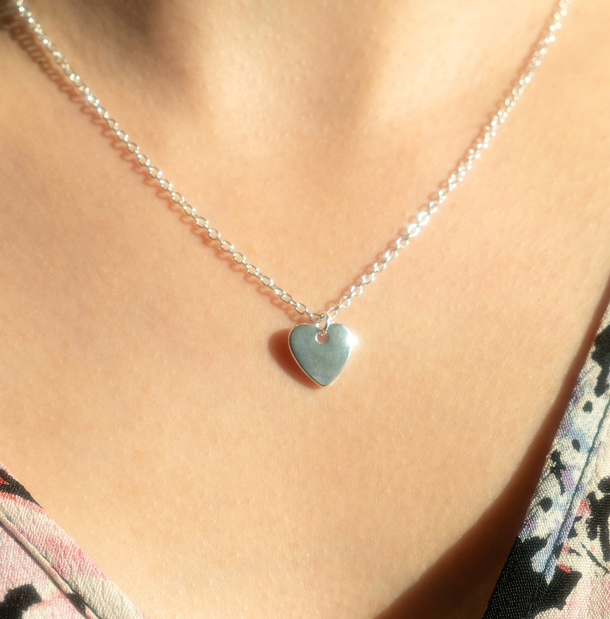 A person wears a silver chain necklace with a heart pendant.