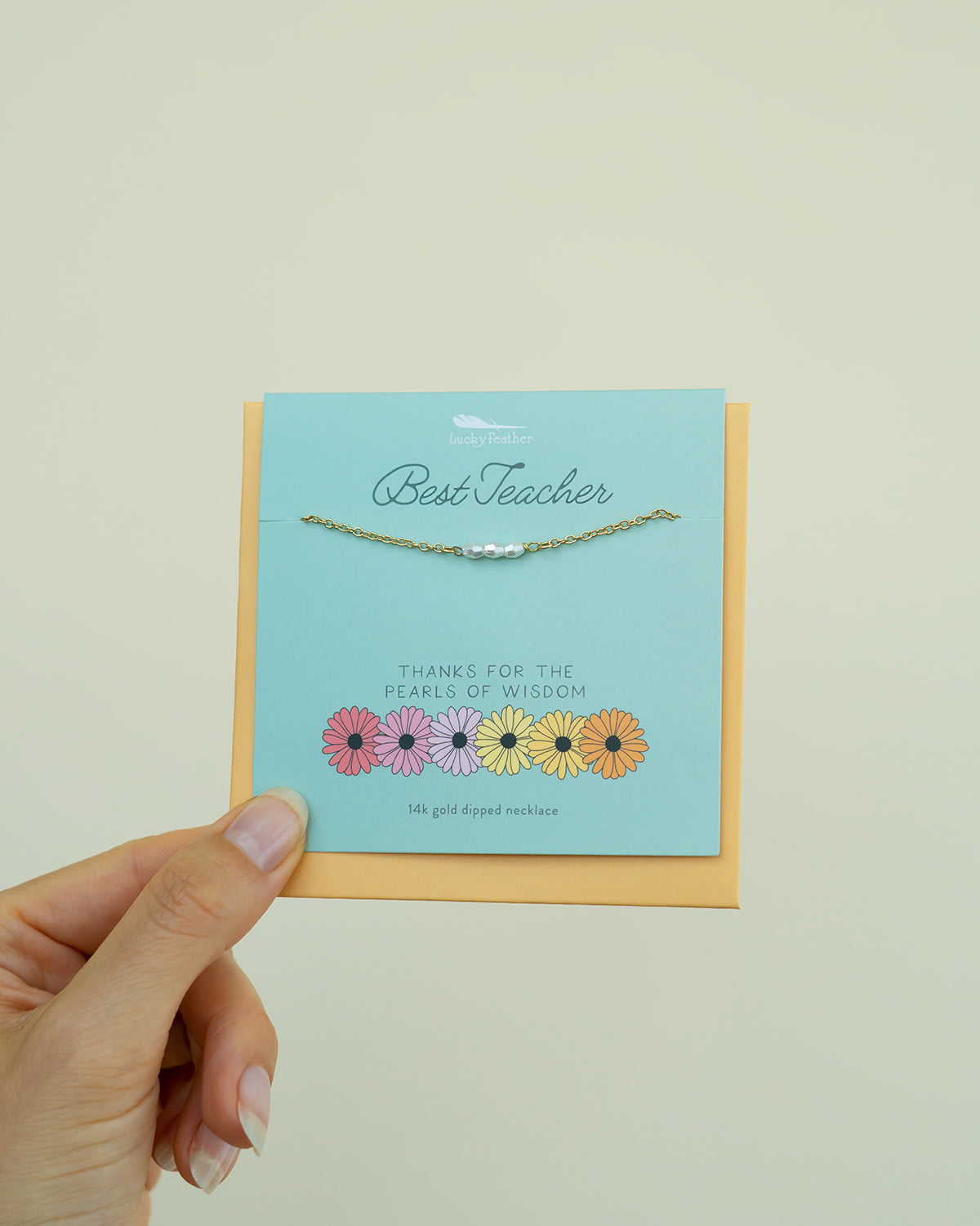 A hand holds a card that displays a gold necklace with pearls, a "Best Teacher" message, and flower illustrations.