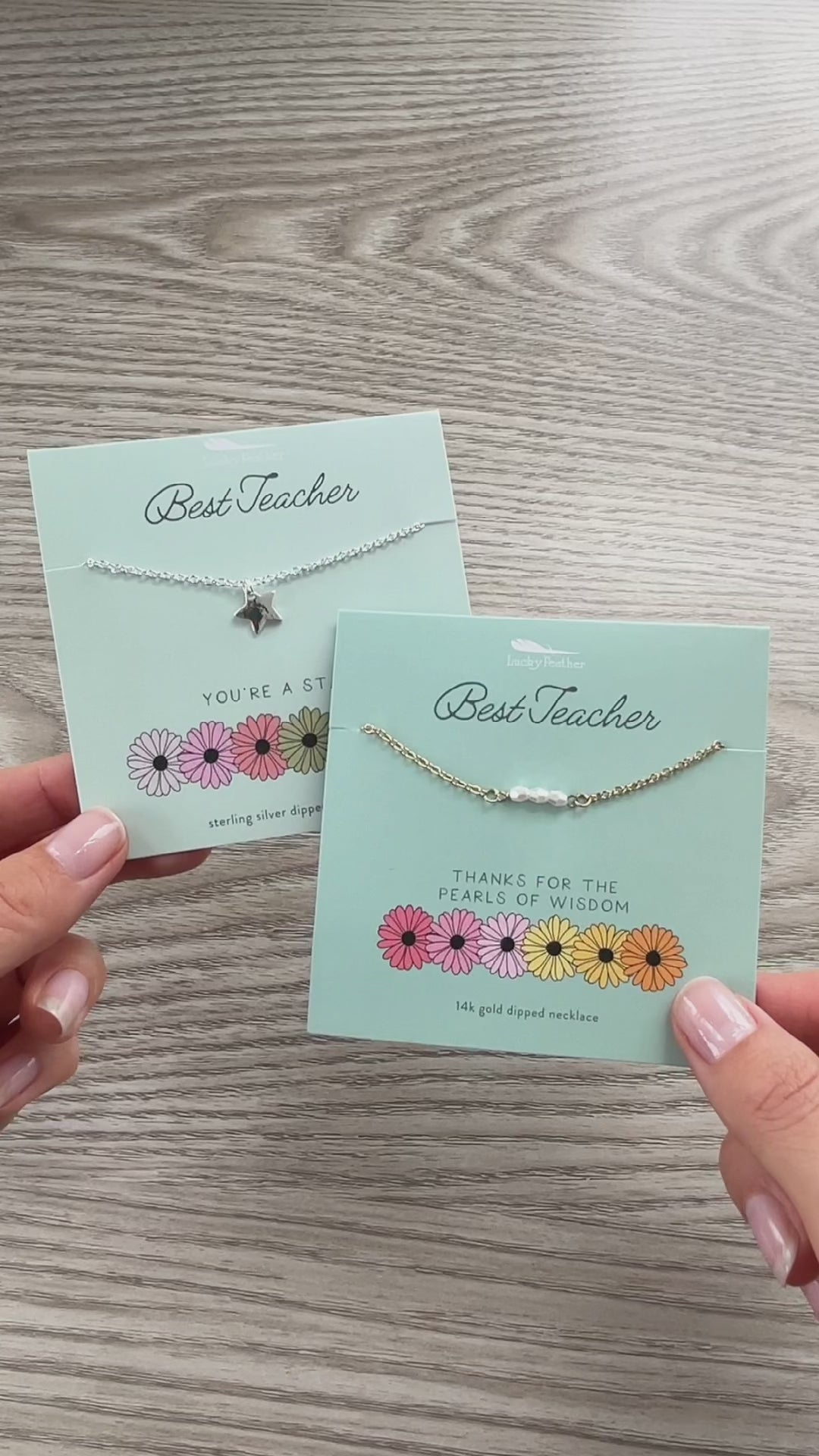 Two hands hold necklaces presented on cards with the words 'Best Teacher'.