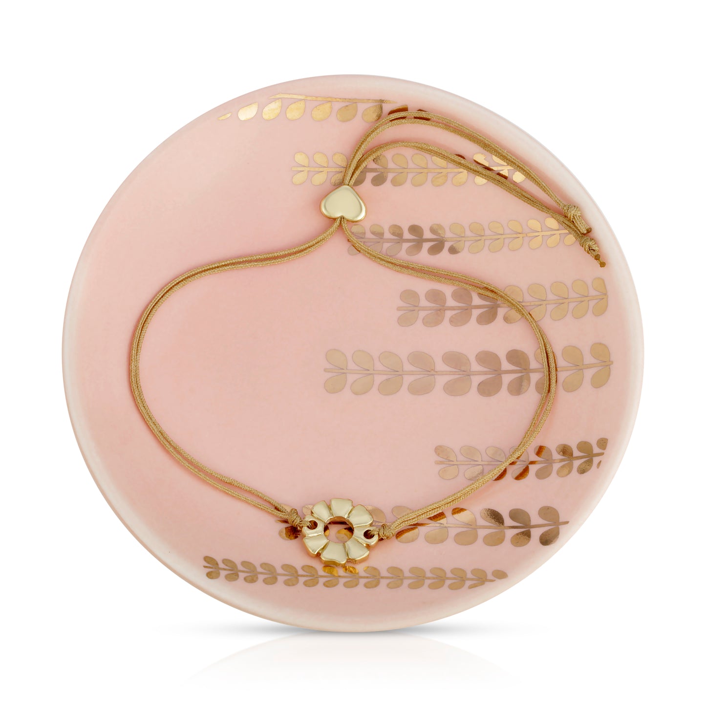 A gold-tone bracelet with a flower motif and a heart charm rests on a pink plate decorated with gold leaf designs.
