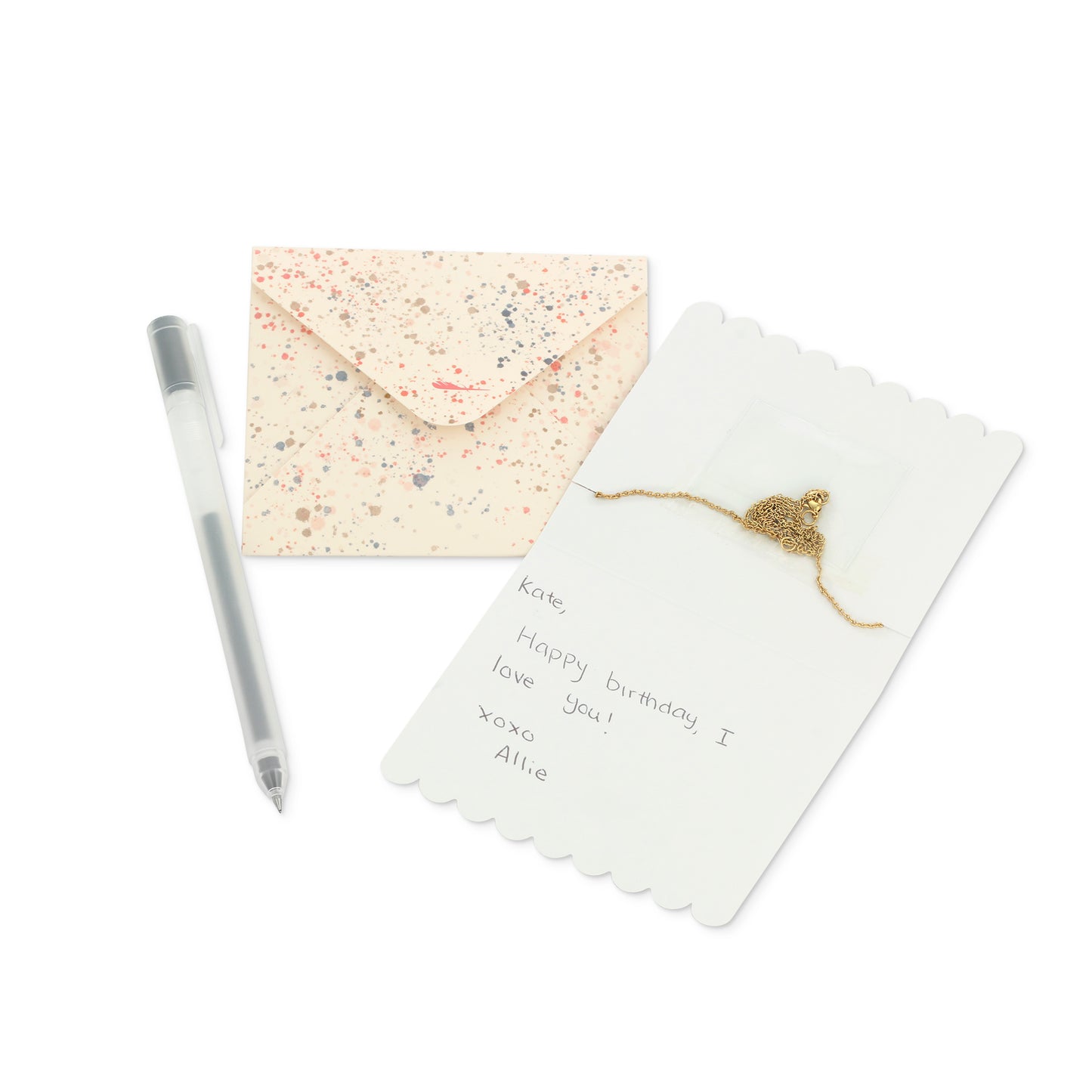 A pen, envelope, and card with a gold necklace are arranged on a white background.