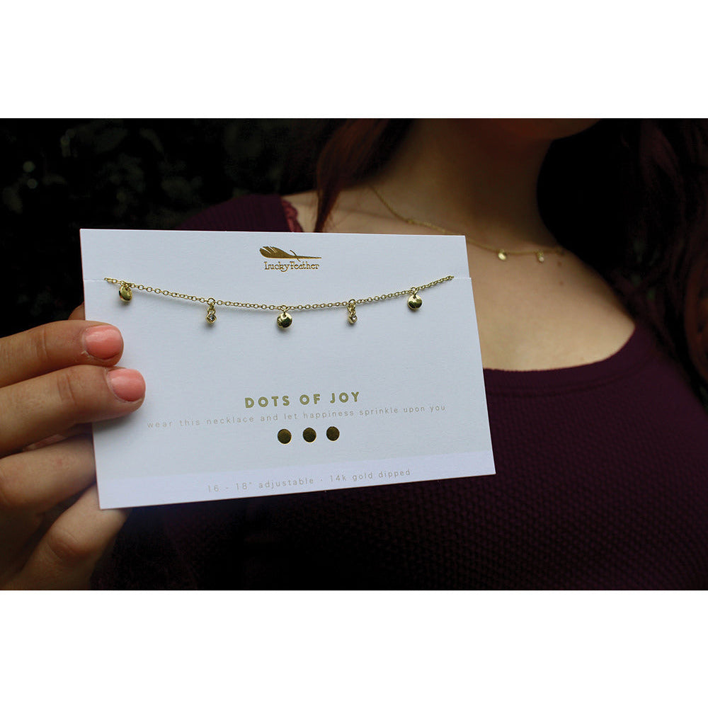 A woman models a Lucky Feather "Dots of Joy" necklace on its packaging, with another similar necklace worn around her neck.