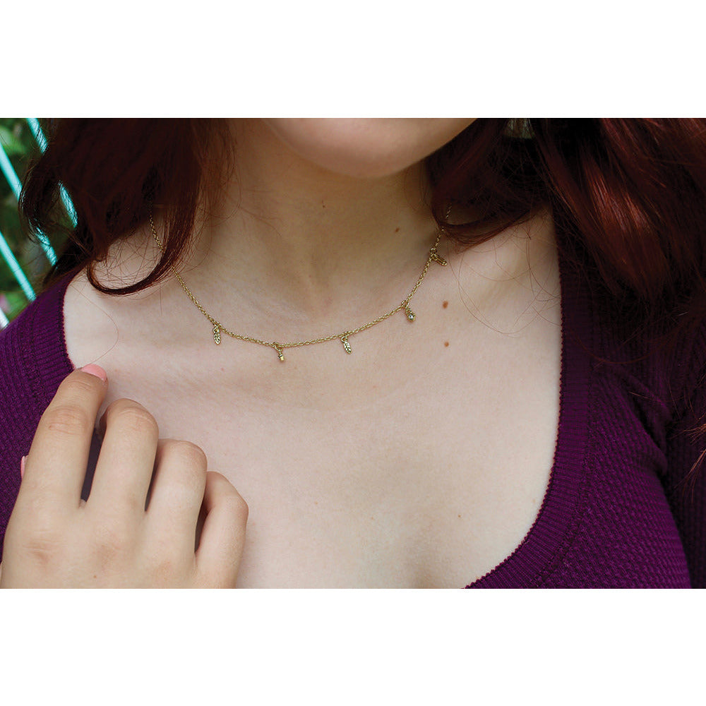A person with red hair and wearing a purple shirt is accessorized with a gold chain necklace with small pendants.