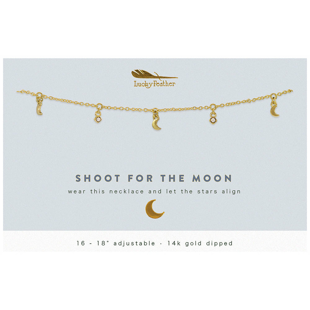 A gold necklace with small moon and gem pendants is displayed on a card that says "Lucky Feather, Shoot for the moon, wear this necklace and let the stars align".