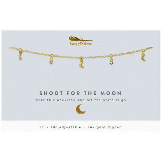 A gold necklace with small moon and gem pendants is displayed on a card that says 'Lucky Feather, Shoot for the moon, wear this necklace and let the stars align'.