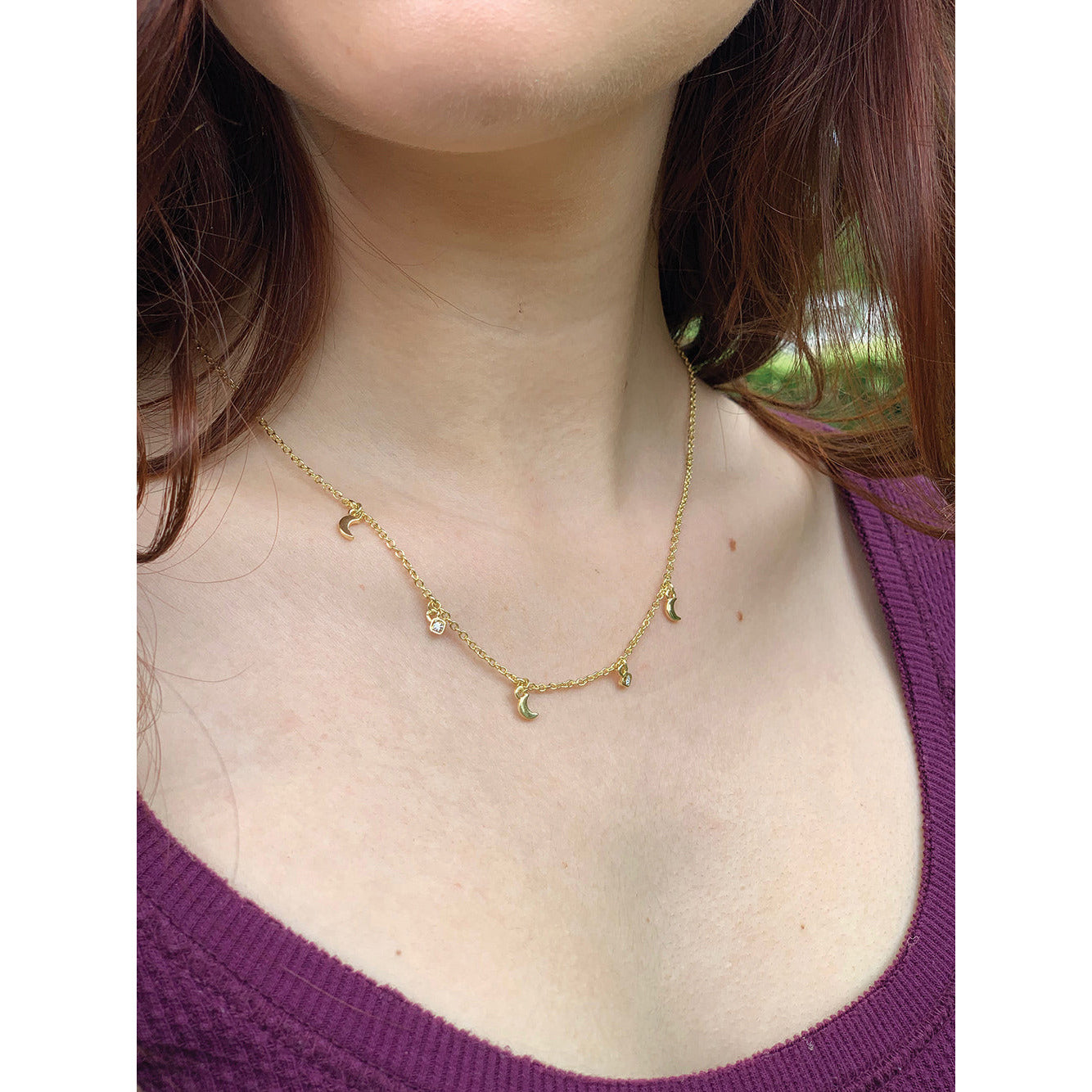 A woman wearing a gold necklace with moon and star charms.