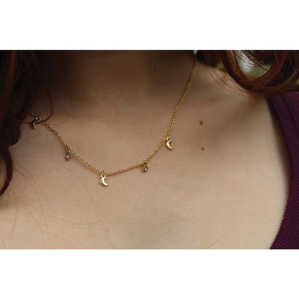 Close-up of a gold necklace with moon and crystal charms worn by a person.
