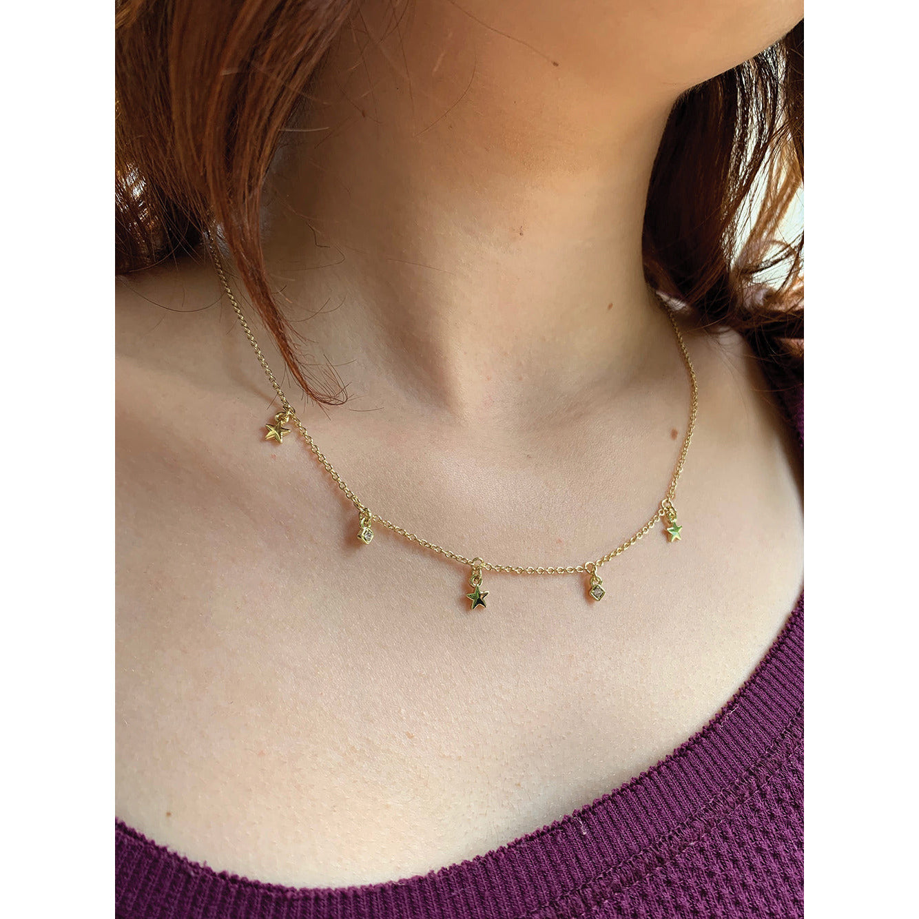 A person wears a gold chain necklace with star and gem charms.