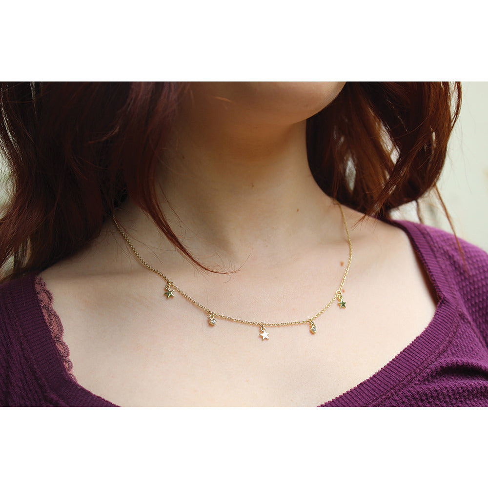 Person wearing a gold chain necklace with hanging stars and jewels.