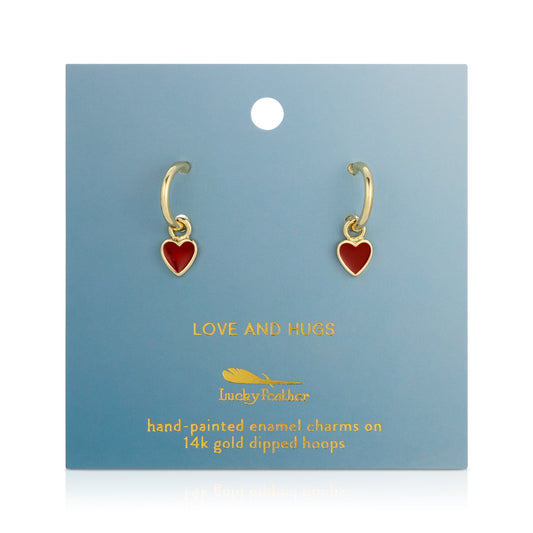 A pair of gold hoop earrings with red heart charms are displayed on a blue card with gold text.