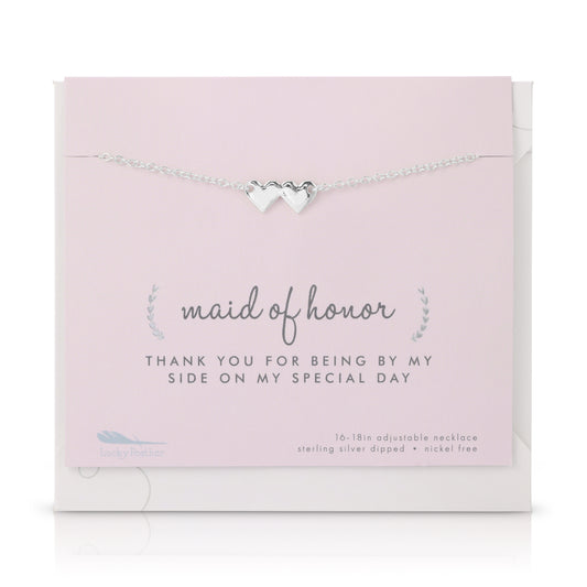 A silver necklace with two hearts is displayed on a pink card with 'maid of honor' printed on it.