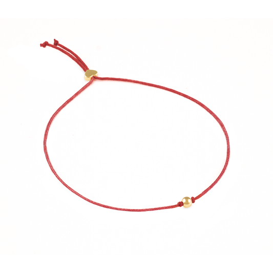 A red string bracelet with a gold bead is displayed on a white background.