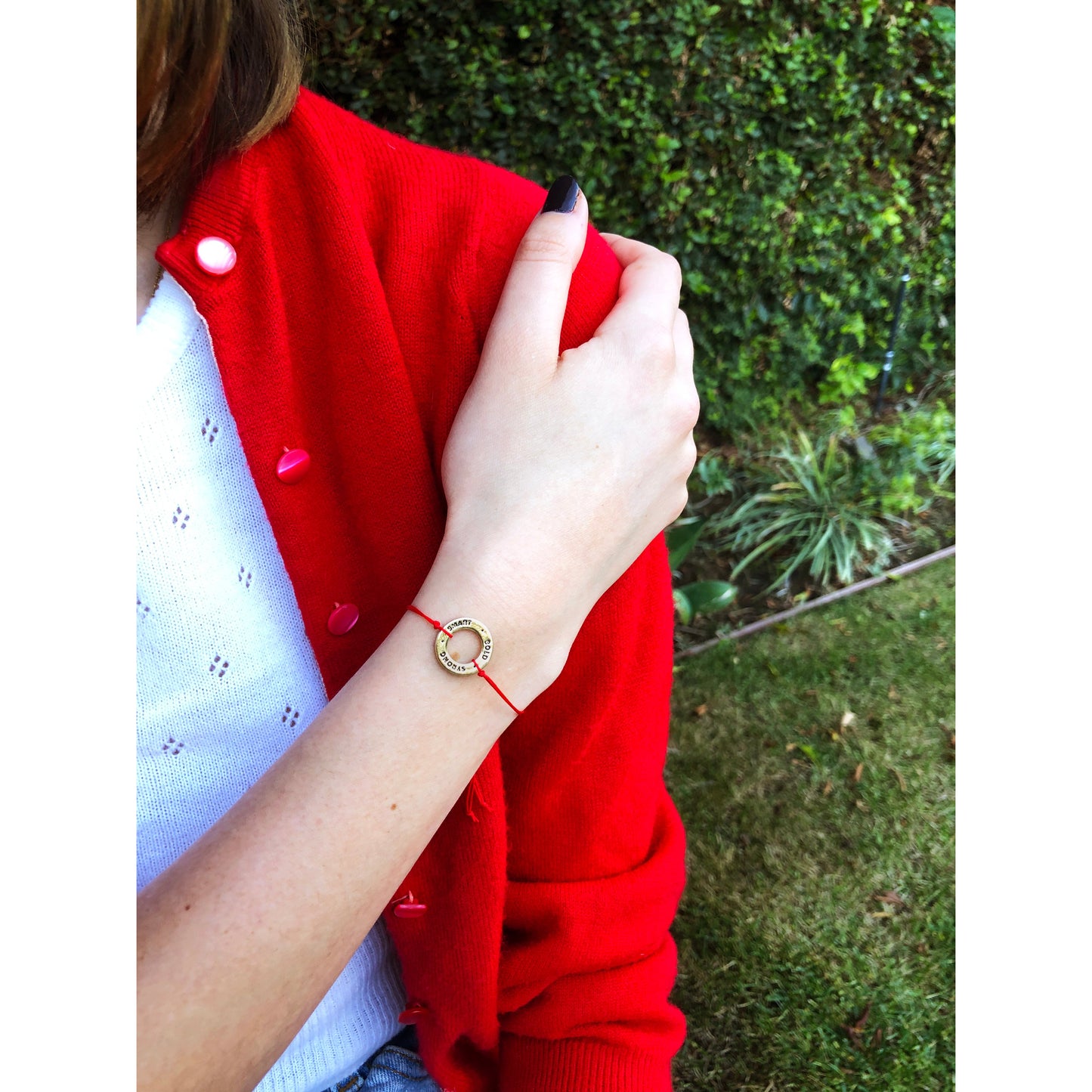 A person with a red cardigan and a "smart, gold, strong" bracelet is standing in front of a green background.