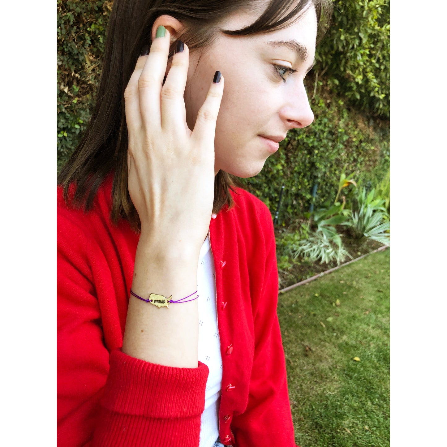 A person in a red cardigan looks to the side, with a purple bracelet featuring a "WRRAP" charm visible on their wrist.