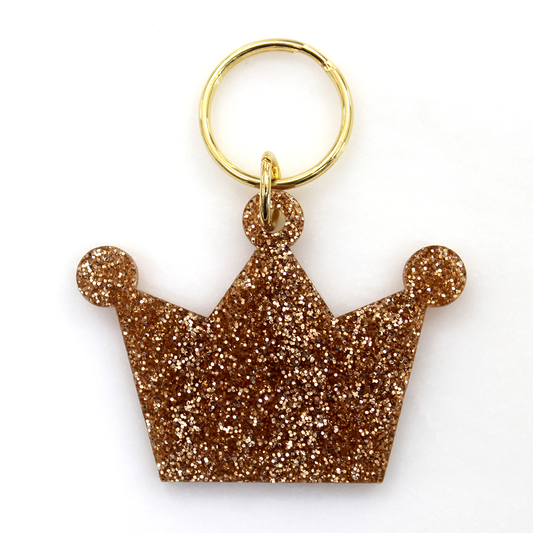 A gold-colored glitter crown keychain is seen against a white background.