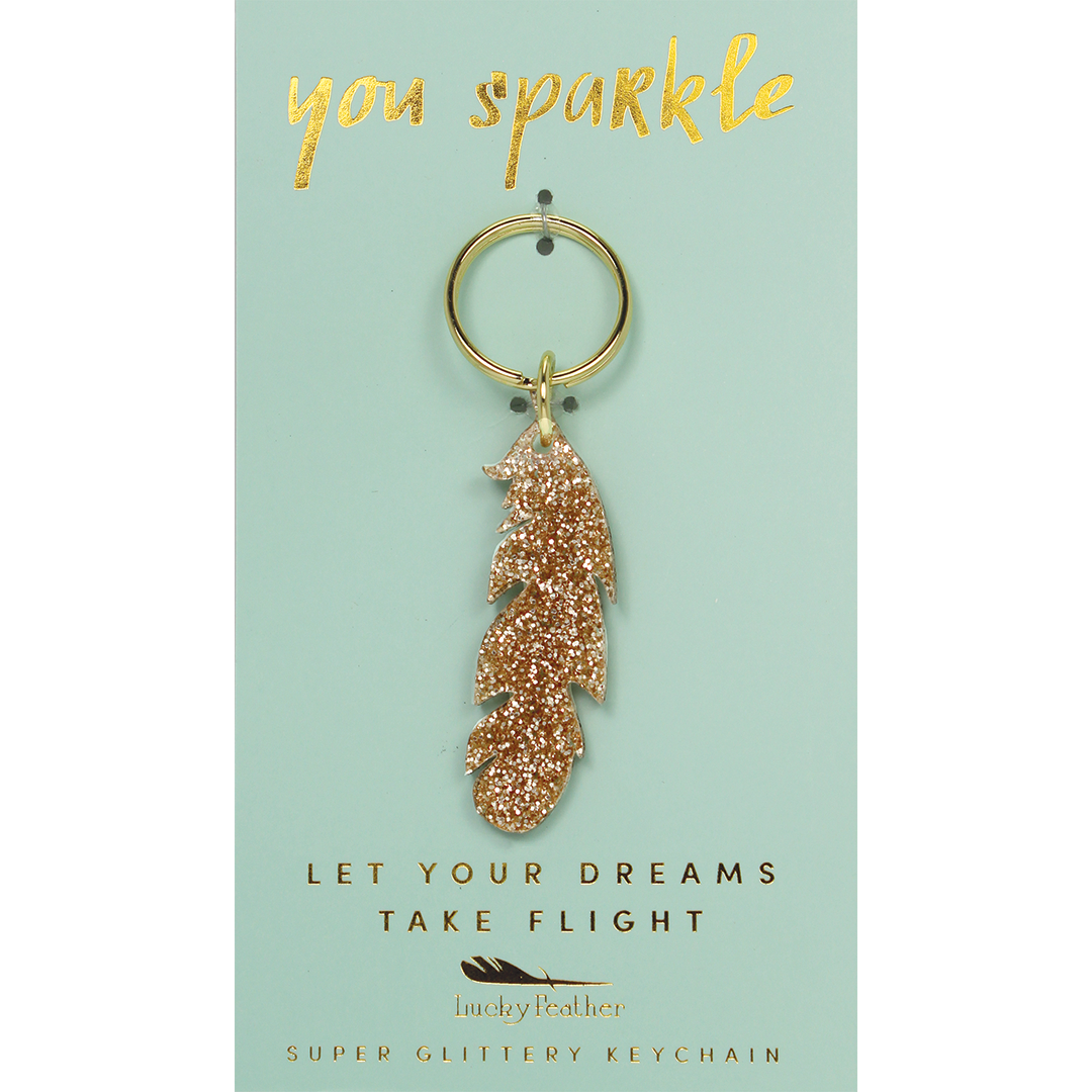 A gold glitter feather keychain hangs on a light blue display card.
