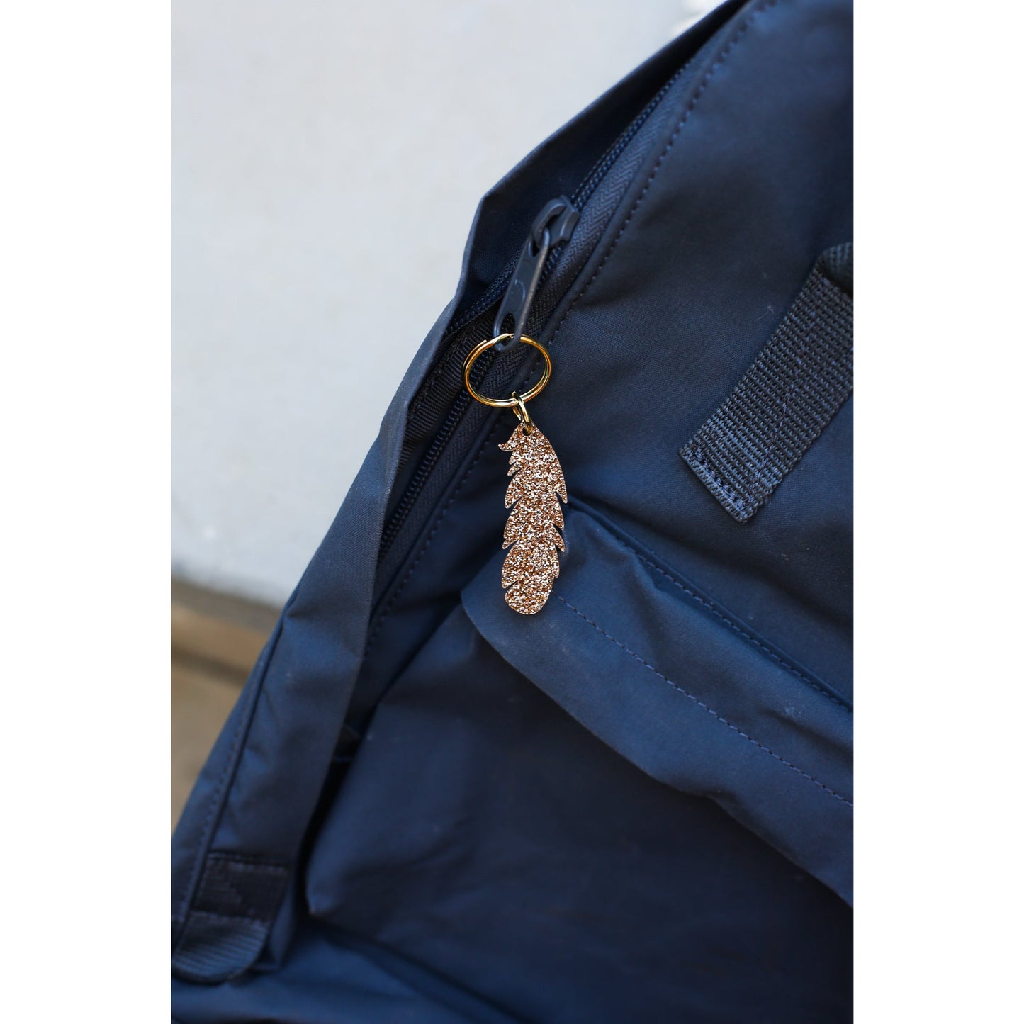 Two smiling women hold up a "Lucky Feather" brand sparkly feather keychain against a blue background.