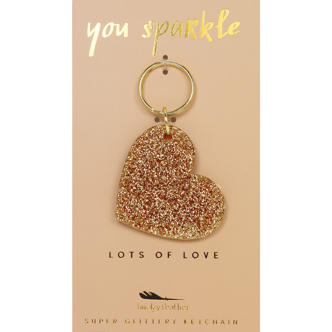 A gold glitter heart-shaped keychain hangs on a display card that says 'you sparkle' and 'lots of love.'