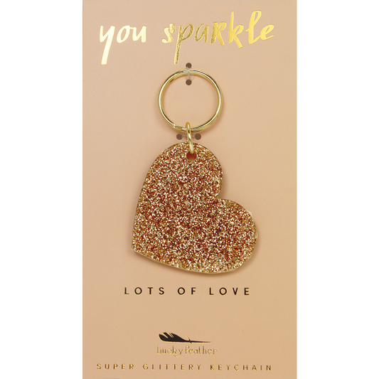 A gold glitter heart-shaped keychain hangs on a display card that says 'you sparkle' and 'lots of love.'