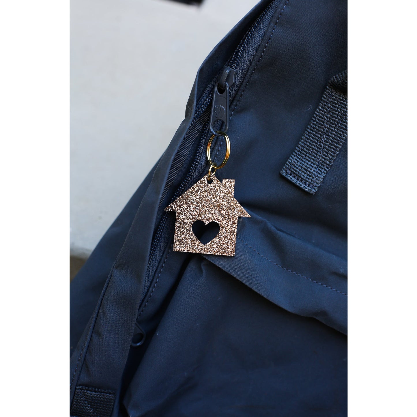 A sparkly gold house-shaped keychain hangs from the zipper of a blue backpack.