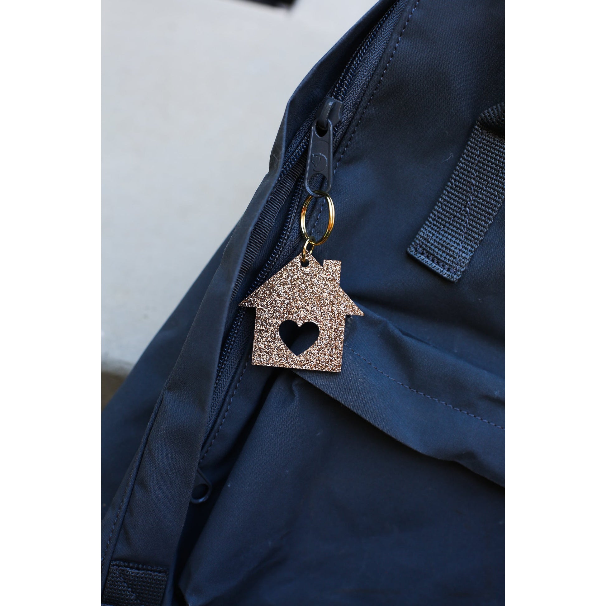 A sparkly gold house-shaped keychain hangs from the zipper of a blue backpack.