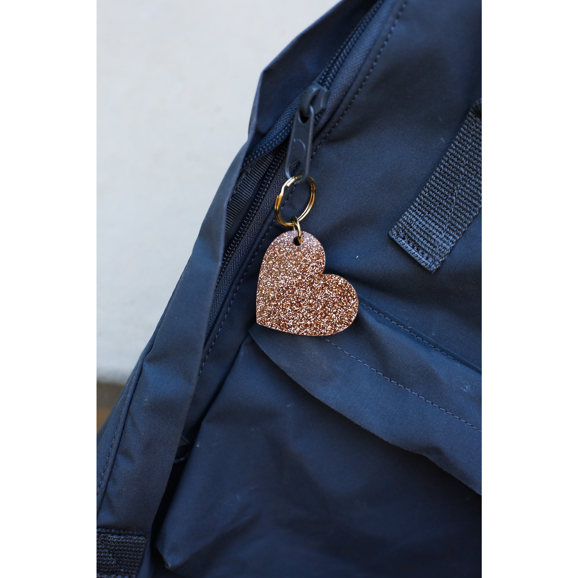 A brown glitter heart keychain hangs from the zipper of a blue backpack.